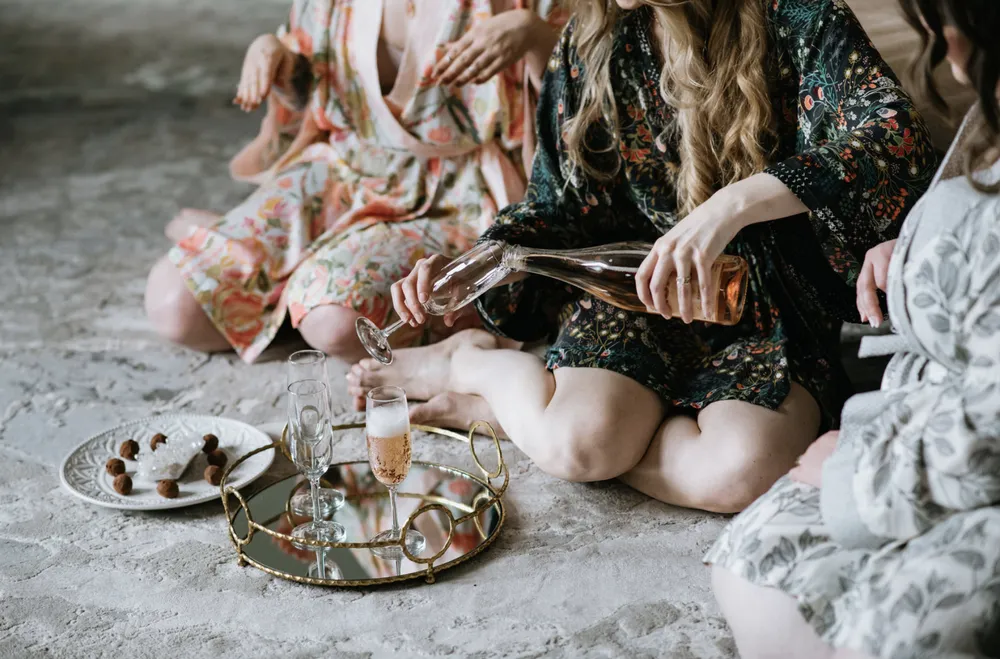 Woman pouring champagne into a glass on a tray with macarons, enjoying a relaxing moment.